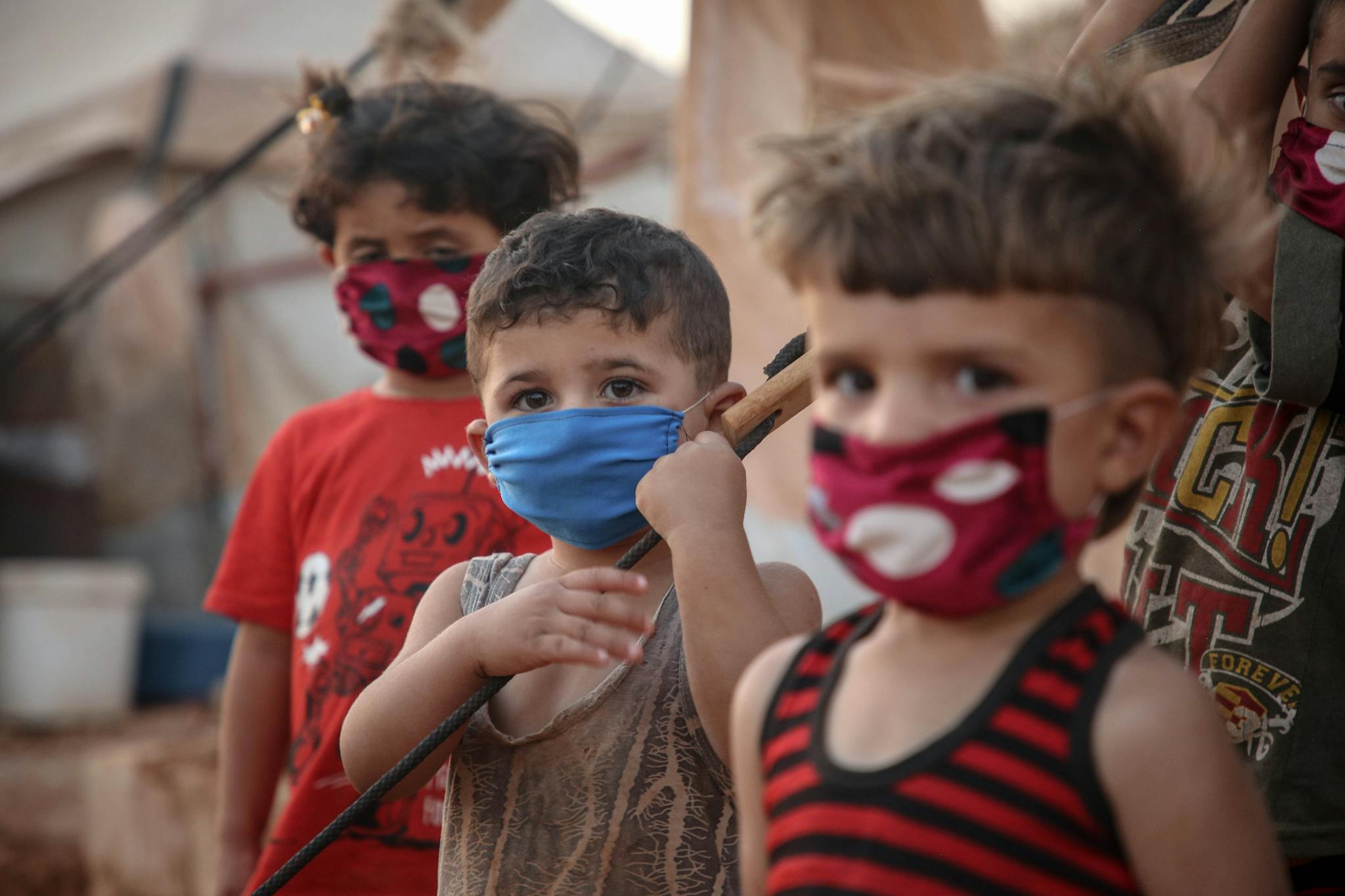 Young children wear face masks in a Syrian refugee camp, illustrating the impact of the pandemic.